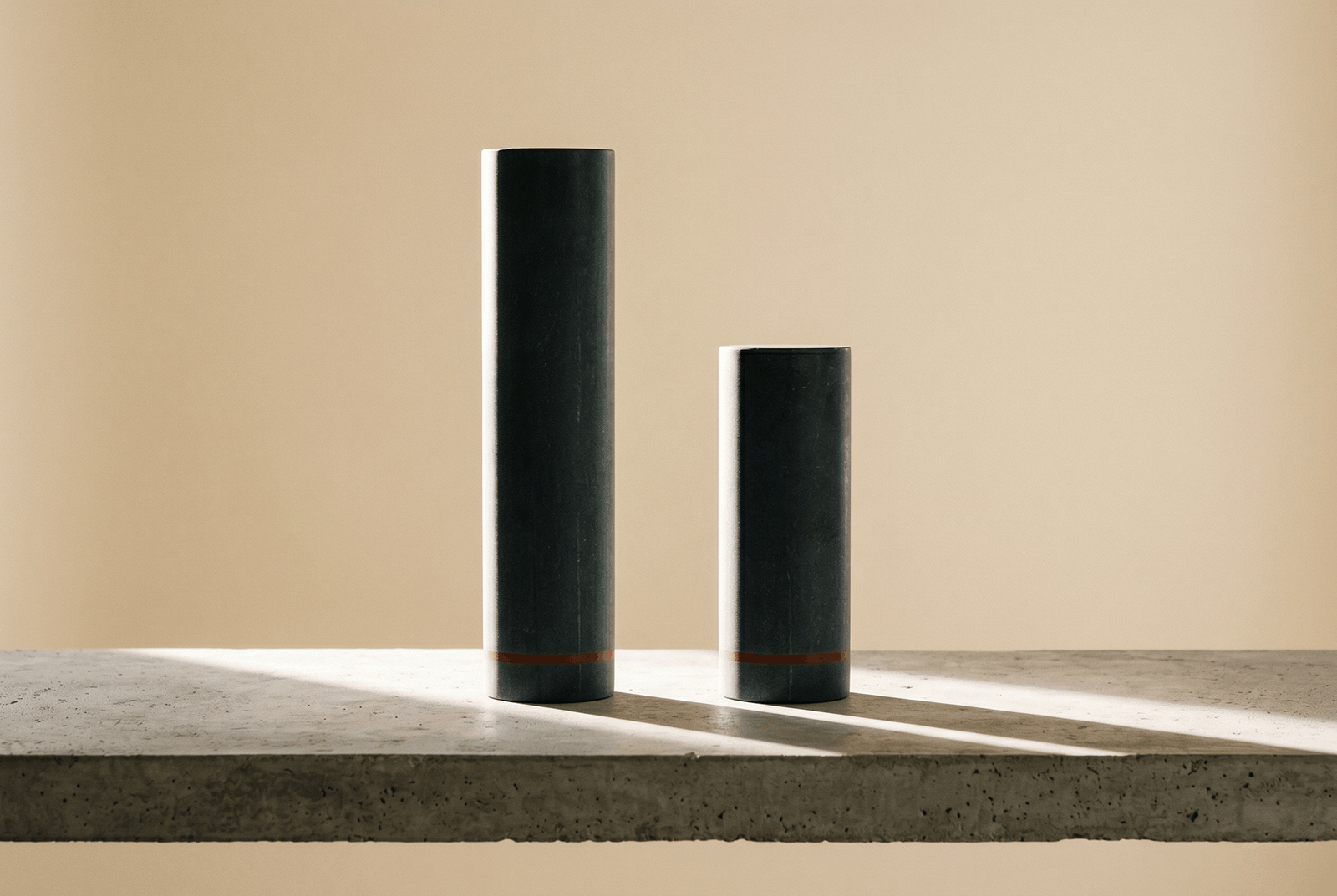 Two dark cylinders of different heights casting long shadows on a concrete surface