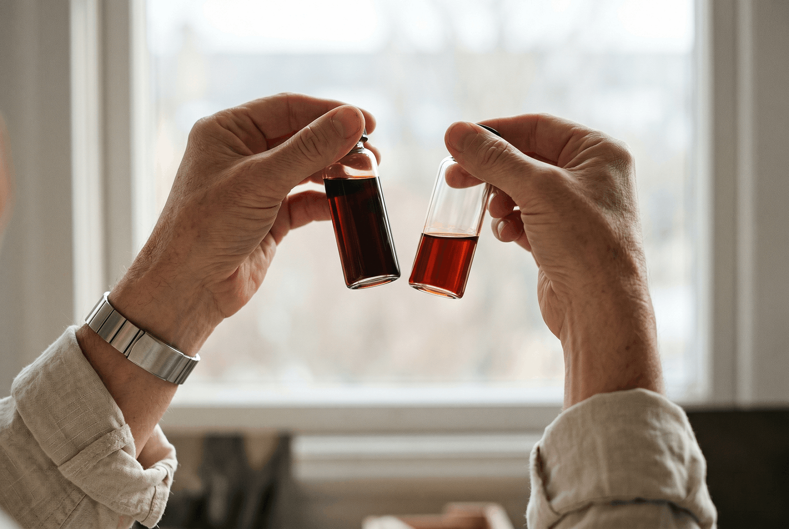 Two hands holding vials of liquid up to the light, comparing concentrations